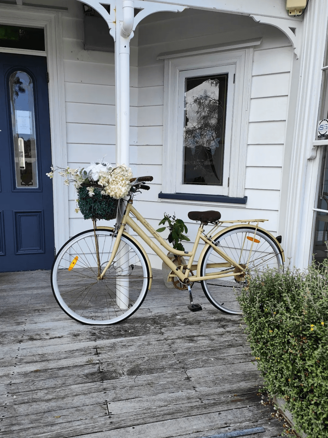 A cream-coloured bicycle with white flowers outside the old house