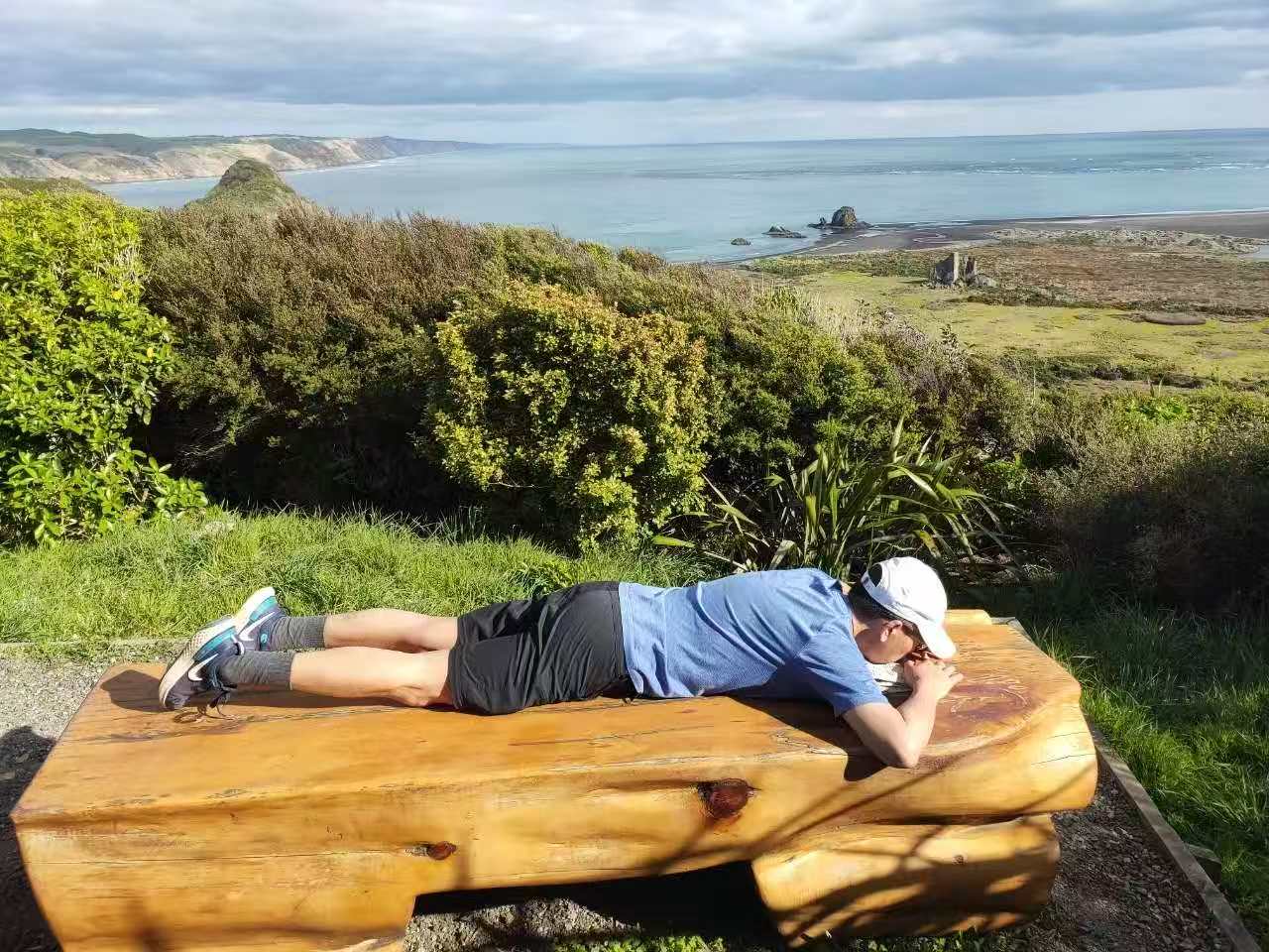 A hiker resting on a bench high above the Whatipū coast