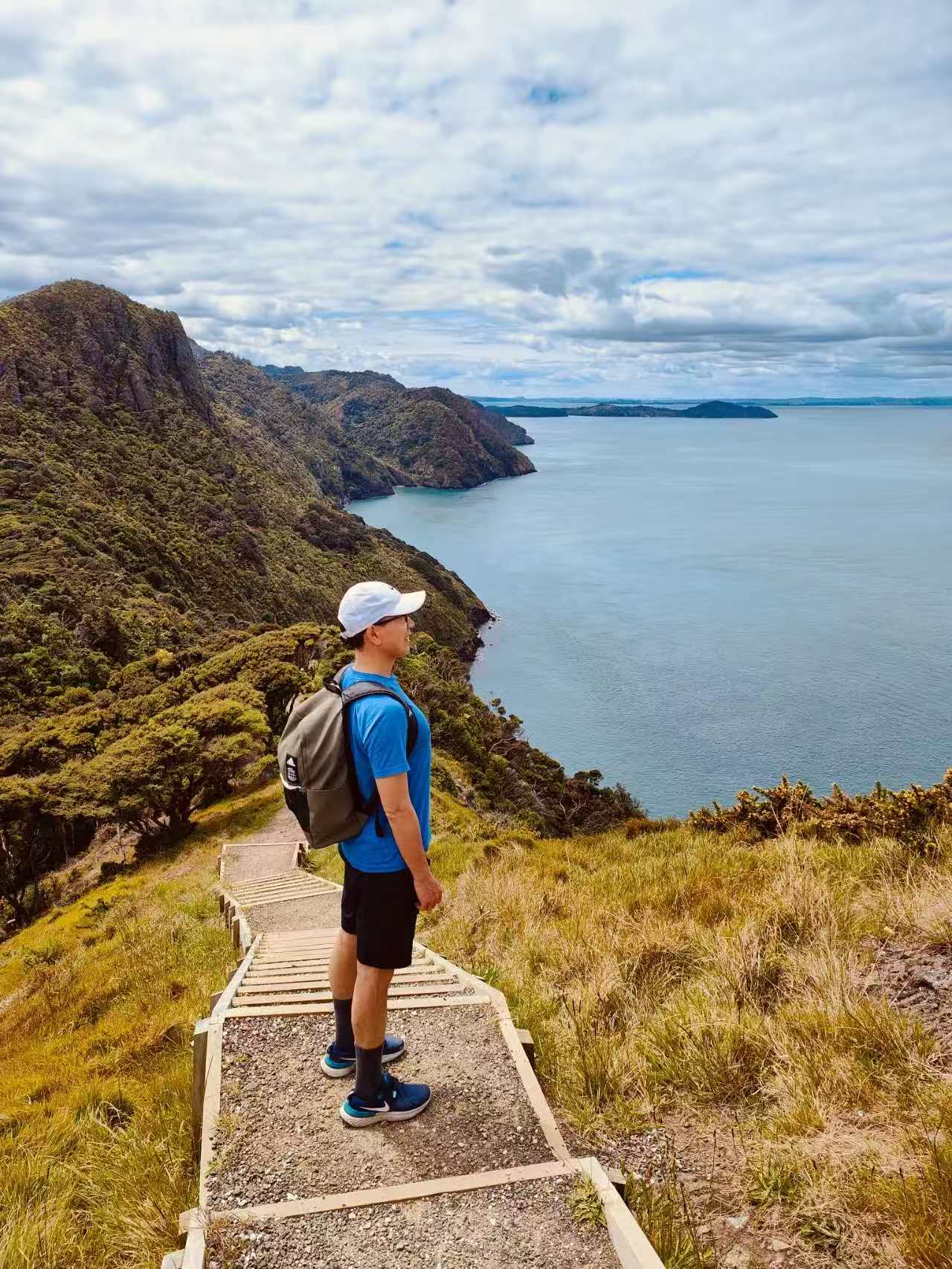 A hiker on the Ōmanawanui ridge above the harbour and the route behind