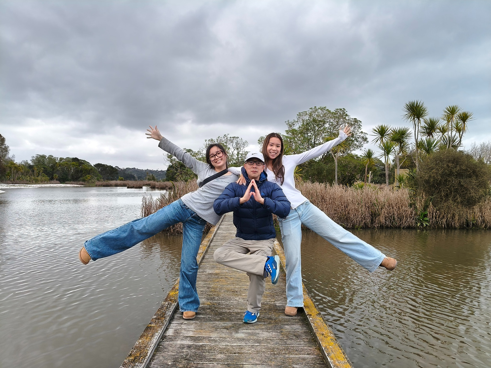 On Father’s Day 2026, a father stands at the centre of the Ayrlies Wetlands boardwalk while his two adult daughters pose behind him with arms and legs outstretched.