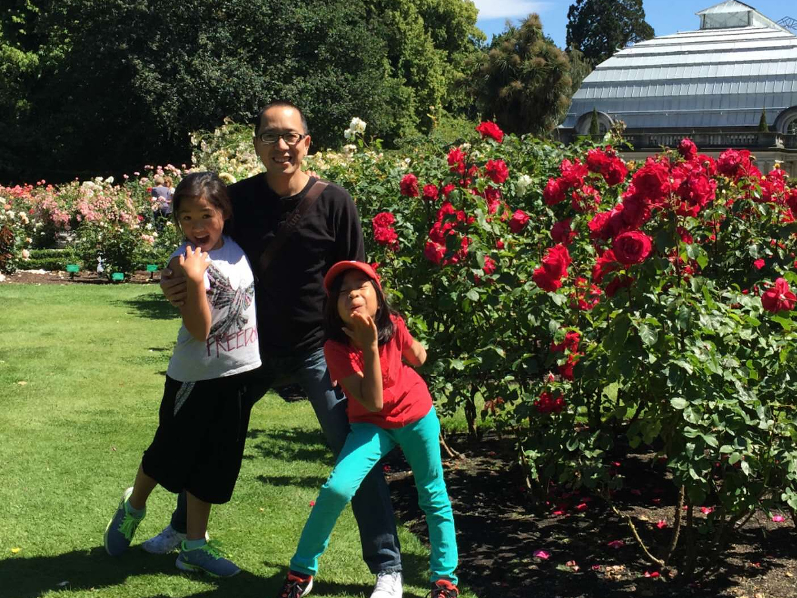 A Father’s Day photograph from many years earlier, with a father standing between his two young daughters in front of flowering rose beds.
